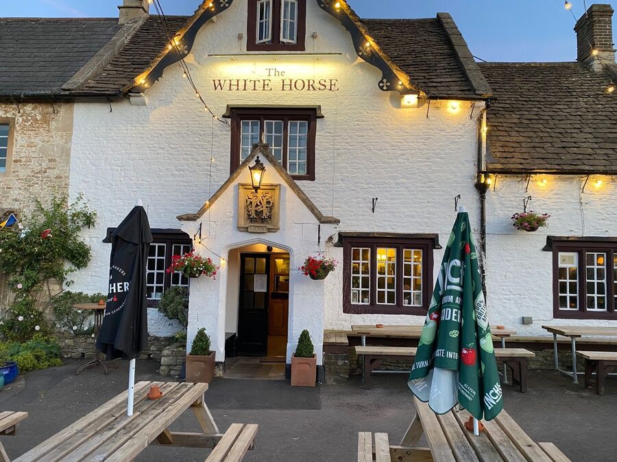 The White Horse at dusk: the limewashed front of the pub with its name painted in burgundy on the gable, strung with festoon lights.
